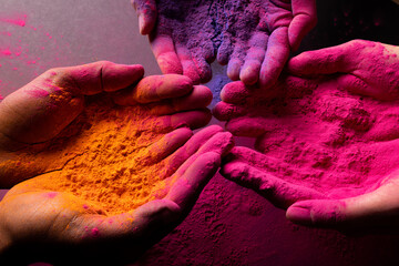 Close up of multi coloured powder on hands over black background