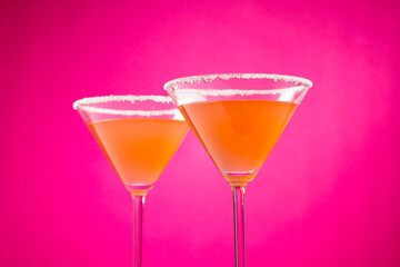 Glasses with cocktail and sugar over neon pink background