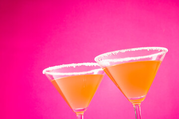 Glasses with cocktail and sugar over neon pink background