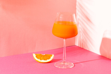Glass with orange juice in pink space with shadows