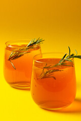 Vertical image of glasses with drinks and thyme over yellow background