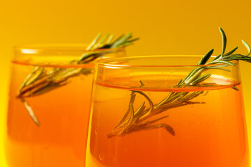 Glasses with drinks and thyme over yellow background