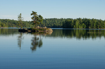 Trees on small island reflected in lake surface