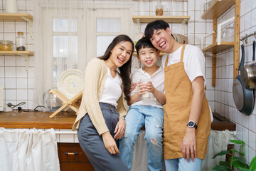 Asian cute little boy having a breakfast with his parent in a kitchen, boy holding a glass of milk and drink.