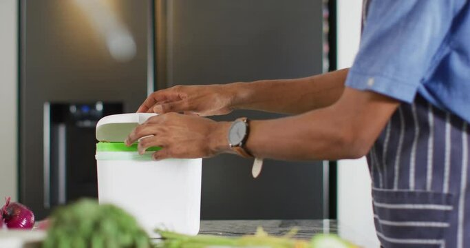 Hands of african american man composting waste in kitchen