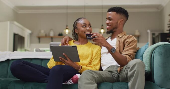 Happy african american couple sitting on sofa and making online shopping