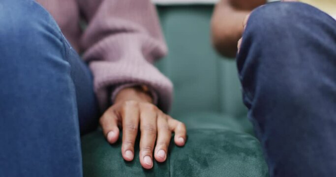 Hands of african american couple sitting on sofa and touching