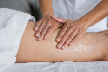 Fototapeta na wymiar Crop masseur applying scrub on leg of client in salon