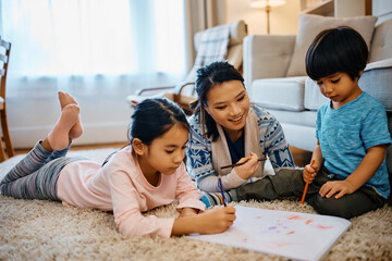 Small Asian kids coloring on paper with their mother at home.