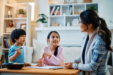 Happy Asian children talk to their mother while drawing on paper at home.