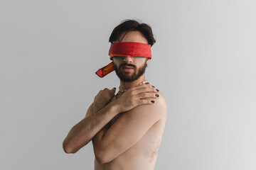Young latin gay queer man with lgbt flag covering his eyes on a white background.