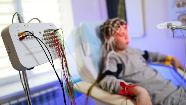 Electrodes attached to the panel and boy sitting at backdrop. Kid is having the brain testing procedure. Blurred background.