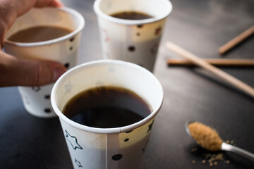 Hand taking a coffe with milk cup and some other coffee cups in some disposable cups on a table in the office	