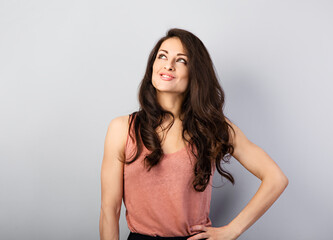 Beautiful thinking makeup toothy smiling woman with long brown healthy hair style looking up. Health care concept. Closeup portrait on blue background