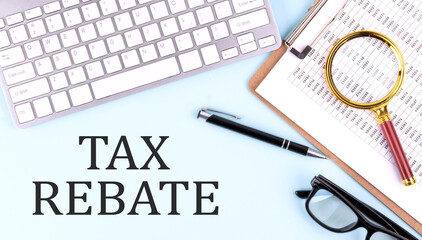 TAX REBATE text on blue background with keyboard and clipboard, business concept