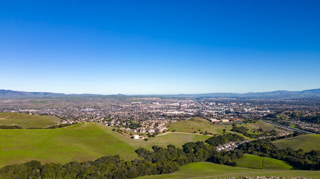 Aerial photos over the Dublin Hills in Dublin, California with a city in the background with a blue sky