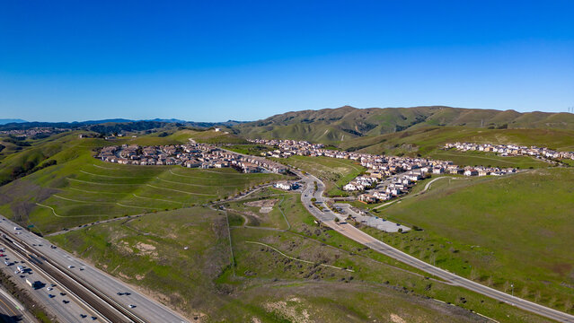 Aerial images over the green hills in Dublin, California with Real Estate in the background and a blue sky