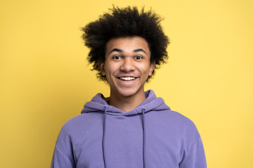 Attractive smiling African American guy wearing stylish purple hoodie isolated on yellow background, positive emotions. Portrait of young happy student looking at camera