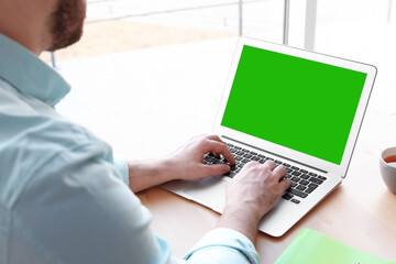 Young man using laptop at desk, closeup. Device display with chroma key