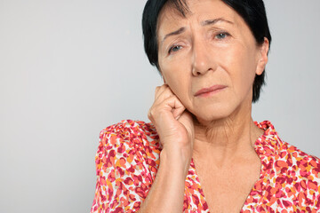 Senior woman suffering from ear pain on light grey background, closeup. Space for text