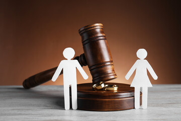 Divorce concept. Gavel, wedding rings and paper cutout of couple on wooden table
