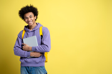 Confident smiling African American student holding laptop isolated on yellow background, copy...