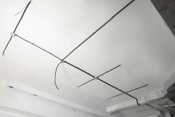 Conduits with cables and ventilation system on white ceiling, low angle view. Installation of electrical wiring