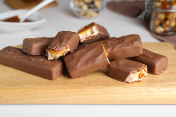 Board with delicious chocolate bars and nuts on white wooden table, closeup