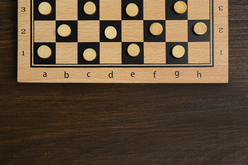Checkerboard with game pieces on wooden table, top view. Space for text