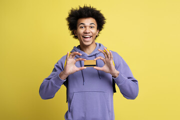 Attractive smiling African American man holding credit card looking at camera isolated on yellow background. Electronic money, shopping, sales concept