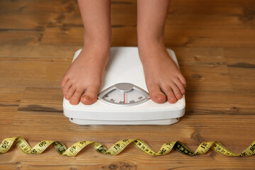 Overweight girl using scales near measuring tape on wooden floor, closeup