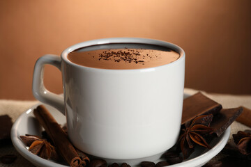 Cup of delicious hot chocolate, spices and coffee beans on table, closeup