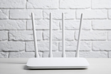 New Wi-Fi router on white wooden table against brick wall