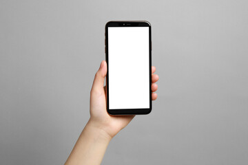 Woman holding smartphone with blank screen on grey background, closeup. Mockup for design