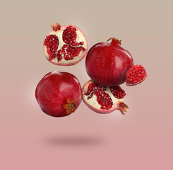 Delicious ripe pomegranate fruits falling on color background
