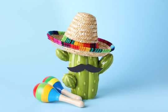 Colorful maracas, toy cactus with sombrero hat and mustache on light blue background. Musical instrument