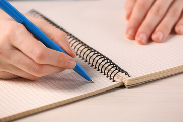Woman writing in notebook at white wooden table, closeup