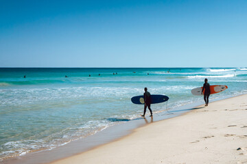 Two surfers walking into the ocean at Scarborough Beach in Perth, Western Australia - obrazy, fototapety, plakaty
