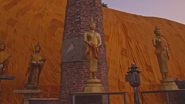 Buddha images in various postures decorated in front of the most beautiful reclining Buddha image in the world..Reclining Buddha at Wat Khun Inthapramun. yellow robe blanket background.