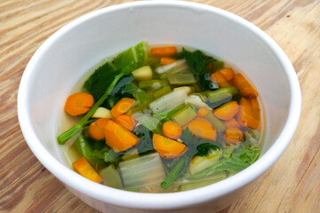 Sayur sop ( Soup) or vegetable soup, is an Indonesian food. Served on white bowl on wooden background, close up.