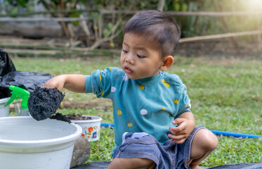 Little child shovels soil into pots to prepare plants for planting. Toddler boy digging soil for...