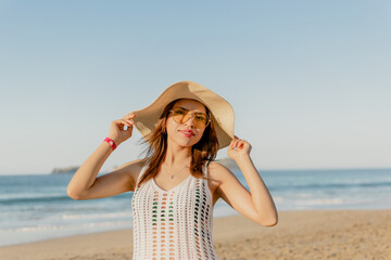 Mujer sonriente tocando su sombrero con ambas manos en la playa