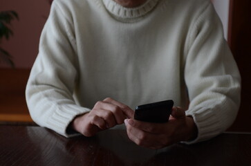 白いセーターを着た男性がスマートフォンを操作しています。