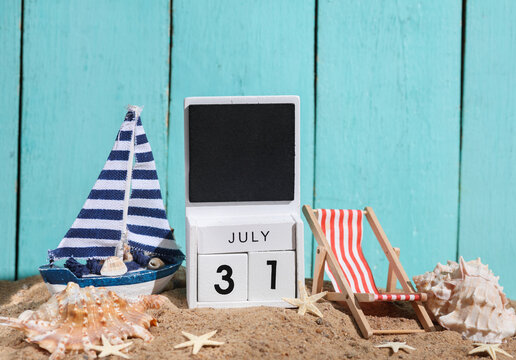 Beach holiday composition with sand, seashells, sailboat, deck chair and wooden block calendar with date july 31. Vacation, summertime, creative travel still life