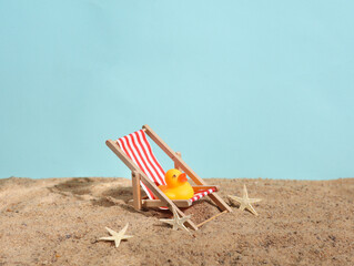 Deck chair with rubber duck on the sand. Beach holiday, summer time