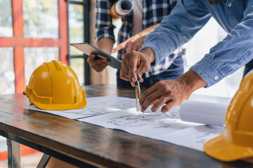 Engineers consulting team close up to design building blueprints paper for clients with building models to work at office.