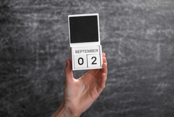 Wooden block calendar with date september 01 in female hand on background of school chalk blackboard