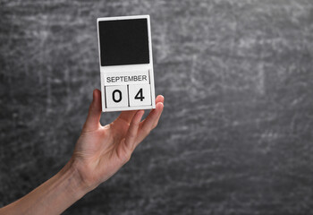 Wooden block calendar with date september 01 in female hand on background of school chalk blackboard