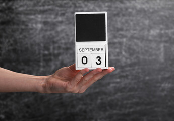 Wooden block calendar with date september 03 in female hand on background of school chalk blackboard