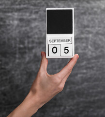 Wooden block calendar with date september 05 in female hand on background of school chalk blackboard